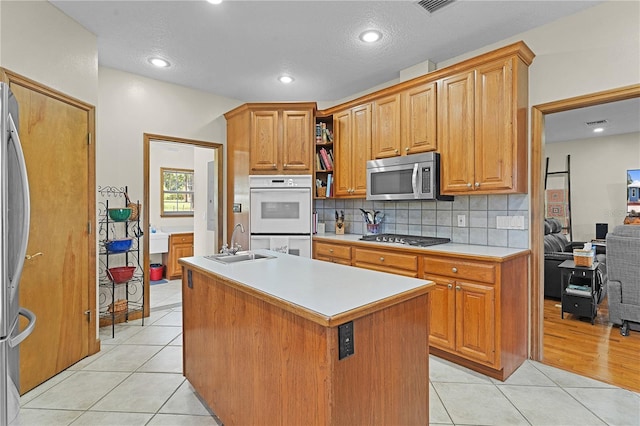 kitchen with sink, light tile patterned flooring, appliances with stainless steel finishes, and a center island with sink