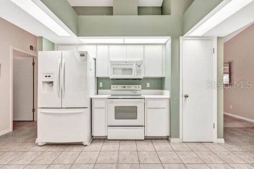 kitchen featuring light tile patterned flooring, white cabinets, a towering ceiling, and white appliances