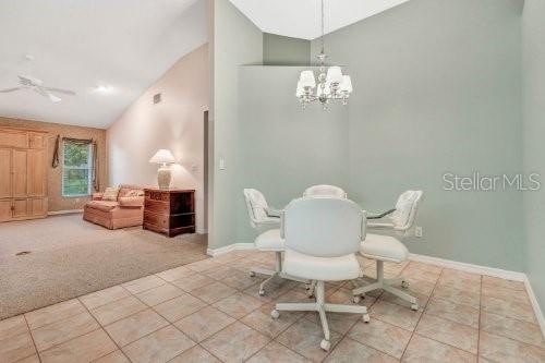 dining space with ceiling fan with notable chandelier, carpet flooring, and high vaulted ceiling