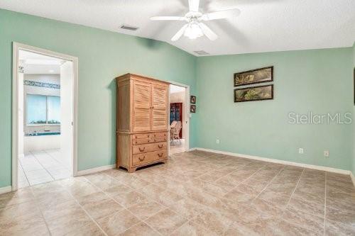 unfurnished bedroom with ensuite bathroom, tile patterned floors, lofted ceiling, and ceiling fan