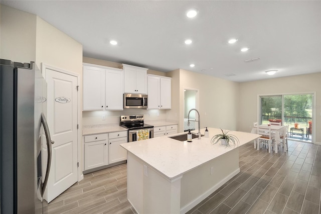 kitchen featuring a kitchen island with sink, white cabinets, sink, light stone countertops, and stainless steel appliances