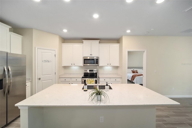 kitchen with a center island with sink, dark hardwood / wood-style floors, light stone countertops, appliances with stainless steel finishes, and white cabinetry