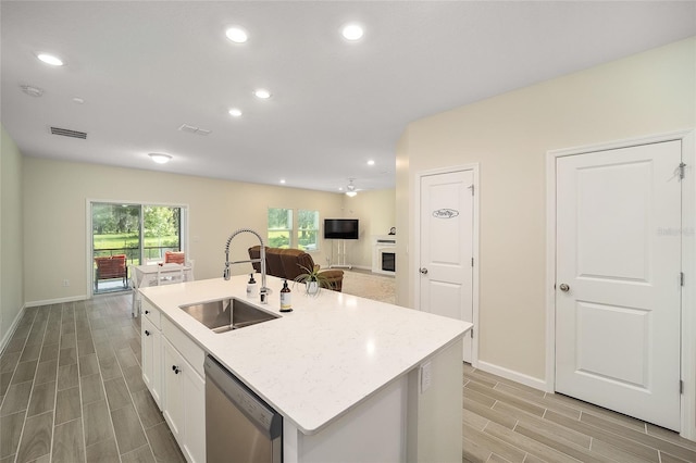 kitchen featuring light stone countertops, sink, dishwasher, white cabinetry, and an island with sink