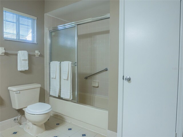 bathroom featuring tile patterned flooring, bath / shower combo with glass door, and toilet