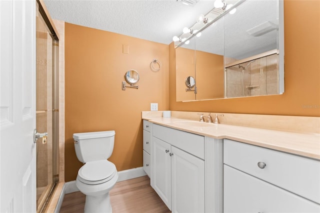 bathroom with hardwood / wood-style floors, vanity, toilet, a shower with door, and a textured ceiling