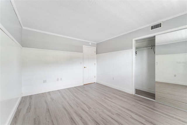 unfurnished bedroom featuring crown molding, light hardwood / wood-style flooring, a closet, and a textured ceiling