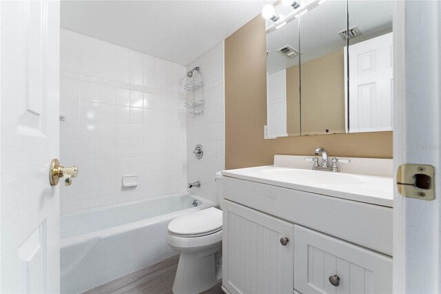 full bathroom featuring vanity, hardwood / wood-style floors, tiled shower / bath, and toilet