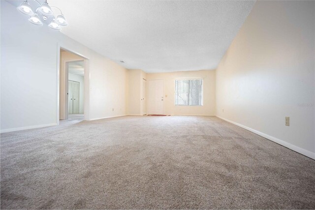 carpeted spare room featuring a textured ceiling and a notable chandelier