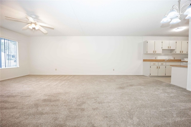 unfurnished living room with sink, ceiling fan with notable chandelier, and light colored carpet