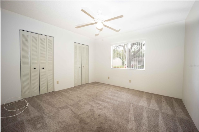 unfurnished bedroom with multiple closets, carpet floors, and ceiling fan