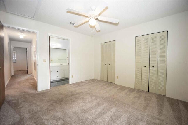 unfurnished bedroom with carpet floors, multiple closets, ensuite bathroom, and ceiling fan