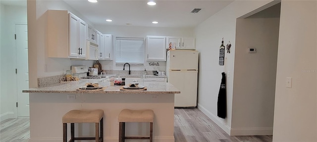 kitchen featuring white appliances, a kitchen breakfast bar, white cabinets, light hardwood / wood-style flooring, and light stone counters