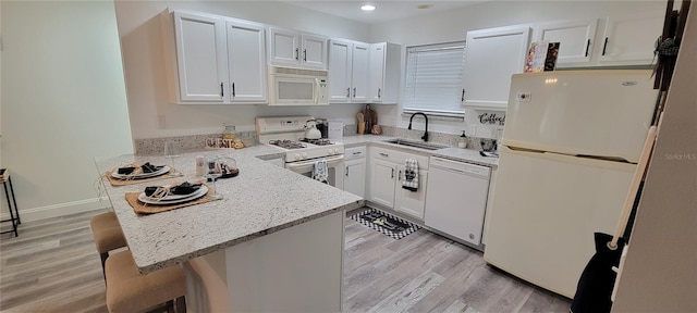 kitchen featuring kitchen peninsula, white appliances, white cabinets, a breakfast bar, and sink