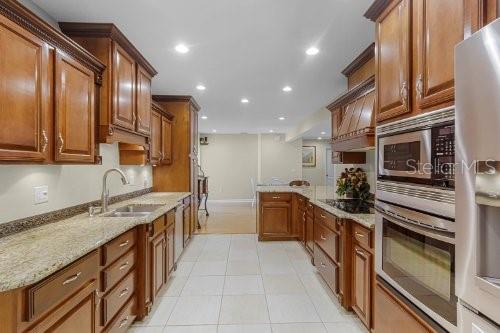 kitchen with stainless steel appliances, sink, light stone counters, light tile patterned floors, and custom range hood