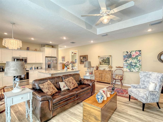 living room with a tray ceiling, light wood-type flooring, and ceiling fan