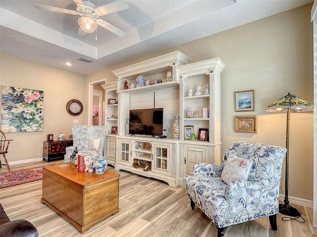 living room with light wood-type flooring, ceiling fan, a raised ceiling, and a textured ceiling