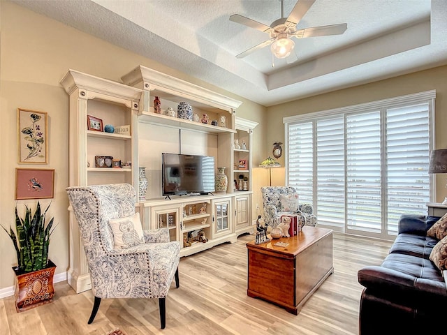 living room featuring a textured ceiling, a raised ceiling, light wood-type flooring, and ceiling fan