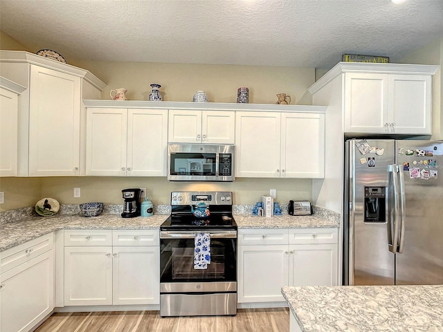 kitchen with white cabinets, stainless steel appliances, light wood-type flooring, and a textured ceiling