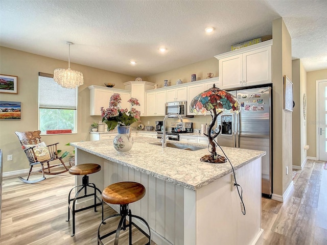 kitchen featuring appliances with stainless steel finishes, light hardwood / wood-style flooring, and a center island with sink