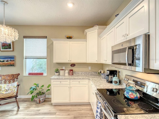 kitchen with a textured ceiling, white cabinets, stainless steel appliances, light hardwood / wood-style floors, and decorative light fixtures