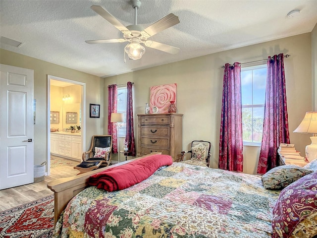 bedroom with light hardwood / wood-style floors, a textured ceiling, ceiling fan, and connected bathroom