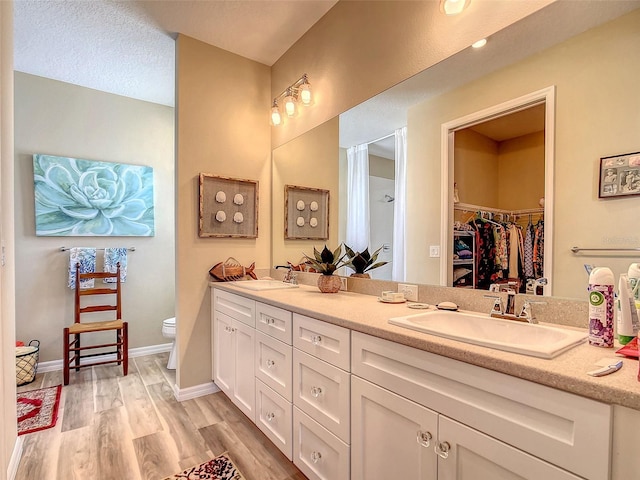 bathroom featuring hardwood / wood-style floors, dual vanity, toilet, and a textured ceiling