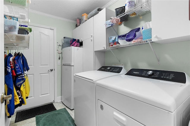 laundry area featuring cabinets, ornamental molding, washing machine and clothes dryer, and a textured ceiling