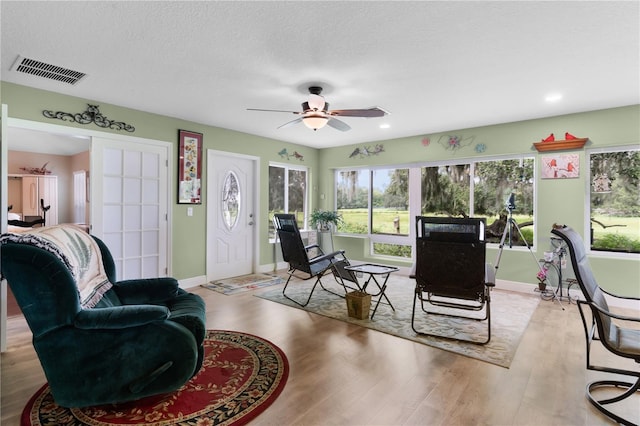 living room with ceiling fan, a textured ceiling, and light wood-type flooring