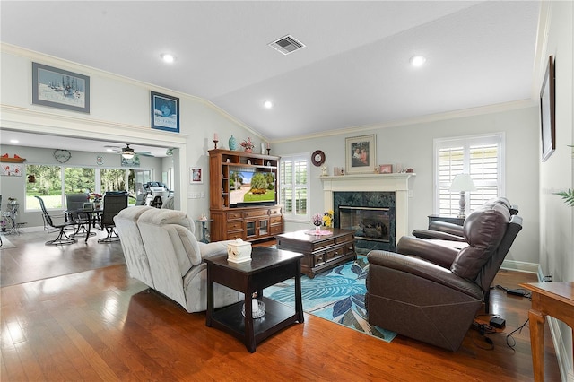 living room featuring vaulted ceiling, hardwood / wood-style floors, ornamental molding, ceiling fan, and a premium fireplace