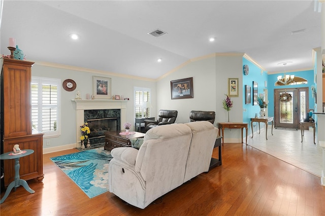 living room featuring crown molding, hardwood / wood-style floors, a notable chandelier, a high end fireplace, and vaulted ceiling