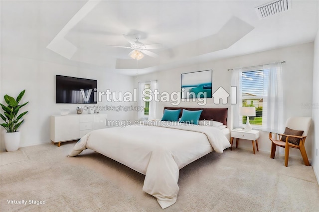 carpeted bedroom with multiple windows, a tray ceiling, and ceiling fan