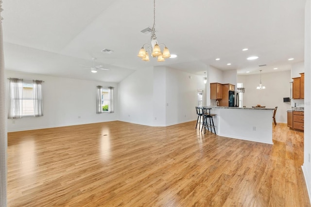 unfurnished living room with ceiling fan with notable chandelier, light hardwood / wood-style flooring, and lofted ceiling