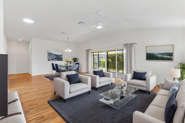 living room featuring hardwood / wood-style floors, ceiling fan with notable chandelier, and vaulted ceiling