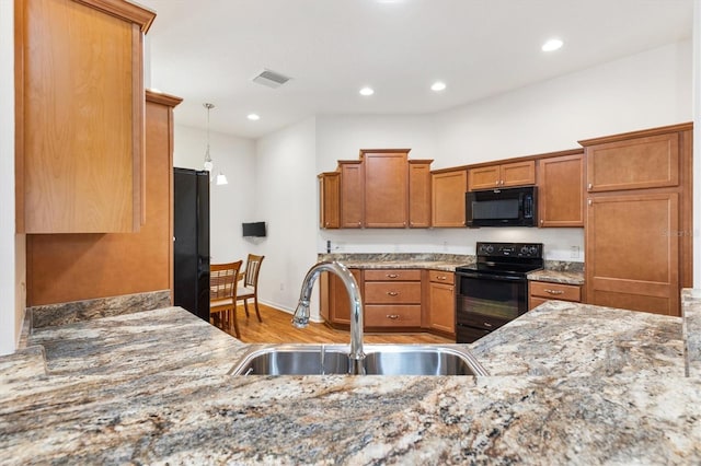 kitchen with pendant lighting, black appliances, sink, light hardwood / wood-style flooring, and light stone countertops