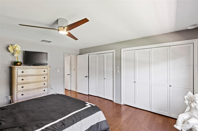 unfurnished bedroom featuring dark wood-type flooring, two closets, and ceiling fan