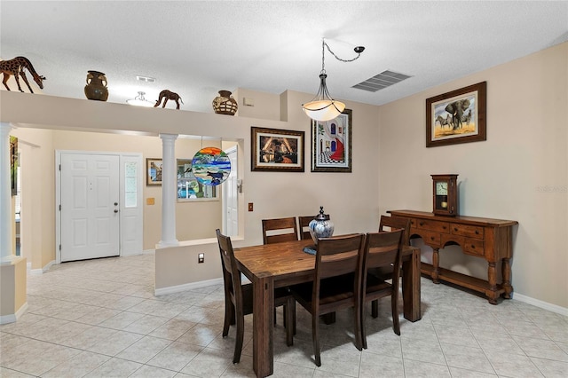 dining room with decorative columns, a textured ceiling, and light tile patterned floors