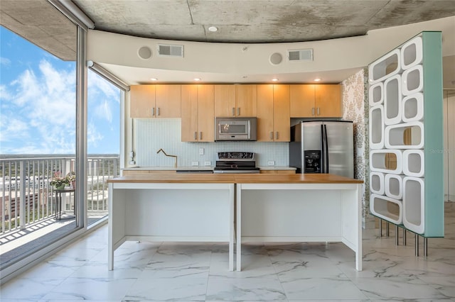 kitchen featuring appliances with stainless steel finishes, butcher block countertops, a breakfast bar area, backsplash, and expansive windows