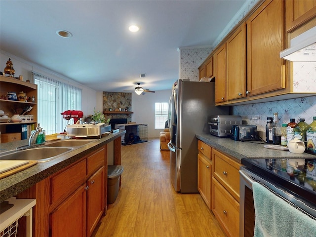 kitchen featuring appliances with stainless steel finishes, a stone fireplace, sink, light hardwood / wood-style floors, and ceiling fan