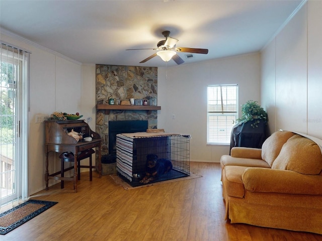 living room featuring ceiling fan, light hardwood / wood-style flooring, and a stone fireplace