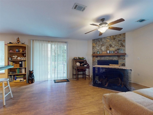 living room featuring hardwood / wood-style flooring, a stone fireplace, and ceiling fan