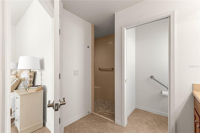 bathroom with a textured ceiling, vanity, and tiled shower