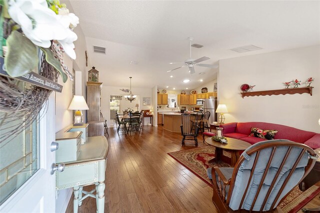 living room featuring hardwood / wood-style flooring, ceiling fan with notable chandelier, and lofted ceiling