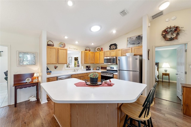 kitchen with appliances with stainless steel finishes, hardwood / wood-style floors, and a kitchen island