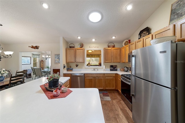 kitchen featuring appliances with stainless steel finishes, hardwood / wood-style floors, an inviting chandelier, sink, and hanging light fixtures