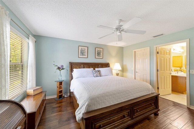 bedroom with ceiling fan, ensuite bathroom, a textured ceiling, and dark wood-type flooring