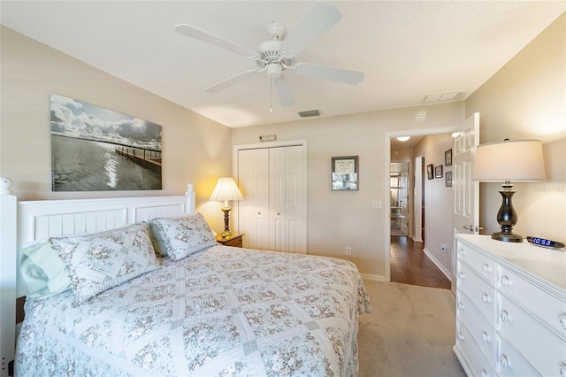 bedroom featuring a closet, light colored carpet, visible vents, a ceiling fan, and a textured ceiling