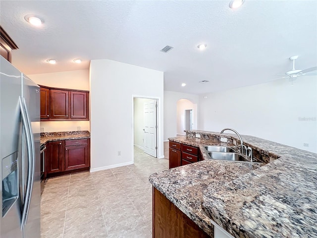 kitchen featuring arched walkways, a sink, dark brown cabinets, dark stone counters, and stainless steel fridge with ice dispenser