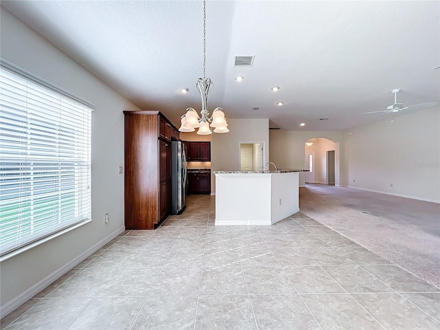 kitchen featuring arched walkways, light carpet, open floor plan, freestanding refrigerator, and decorative light fixtures