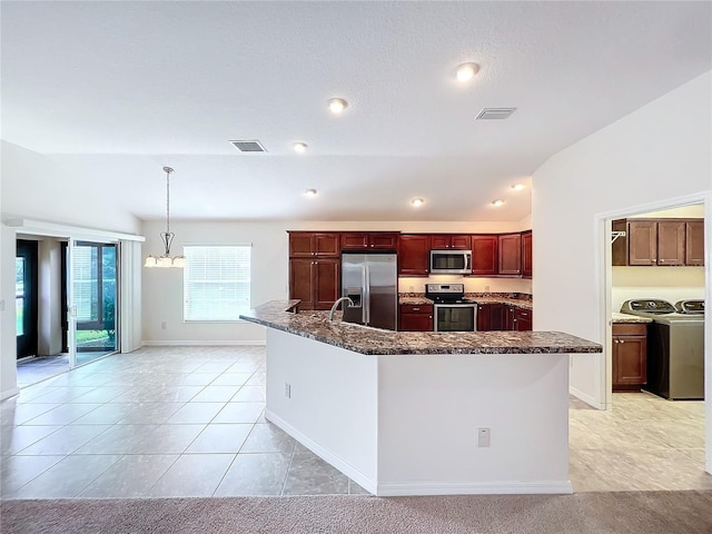 kitchen with lofted ceiling, stainless steel appliances, visible vents, hanging light fixtures, and washer and clothes dryer