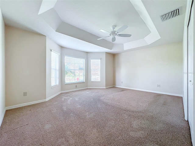 carpeted empty room featuring a ceiling fan, a raised ceiling, visible vents, and baseboards